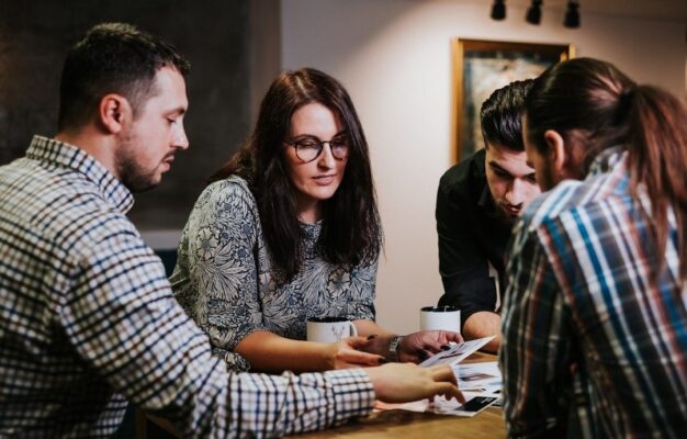 Fyra personer diskuterar dokument vid ett bord under ett redaktionsmöte